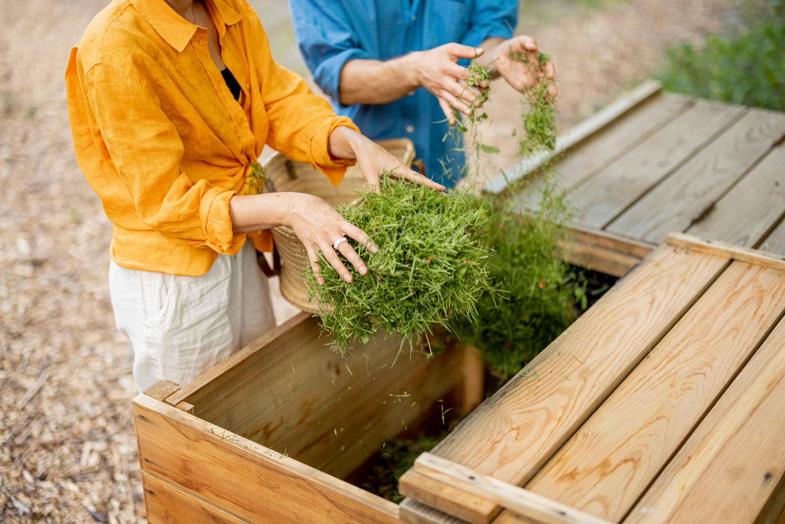 Two people composting plant waste in wooden compost containers